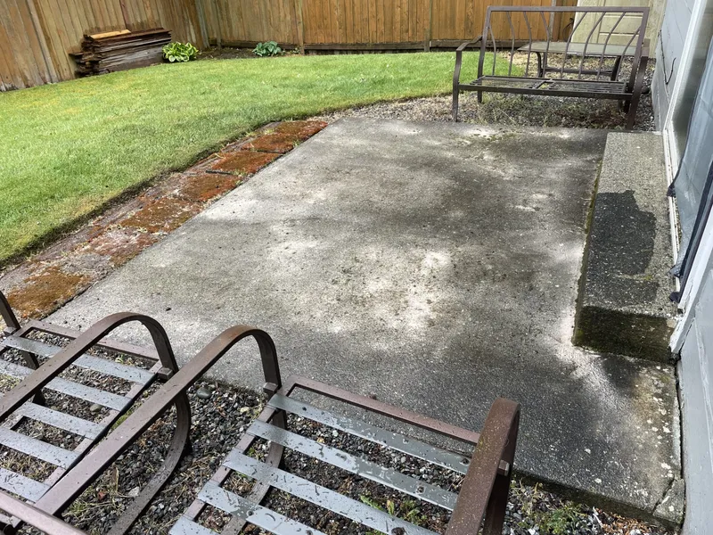A concrete patio streaked with grime and moss along the edges before pressure washing